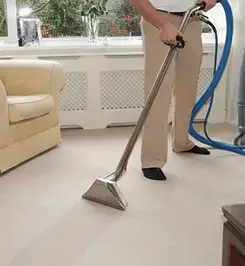 Professional carpet cleaner using a hot-water extraction wand and hose machine in a living room in Henderson, NV.