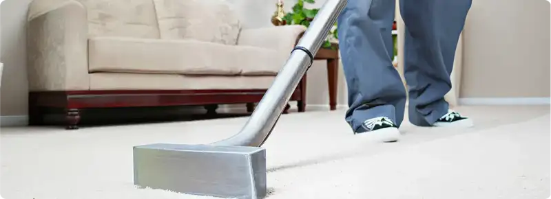 Carpet cleaning technician using a hot-water extraction wand on a light-colored carpet in a living room, Henderson, NV.