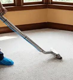Steam carpet cleaning technician using a hot-water extraction wand on a residential carpet, wearing blue protective shoe covers Henderson, NV.