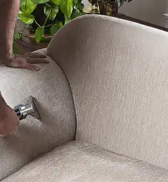 Professional upholstery cleaner deep-cleaning a fabric sofa with a handheld extraction tool and hose Henderson, NV.