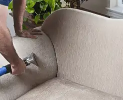 Professional upholstery cleaner deep-cleaning a fabric sofa with a handheld extraction tool and hose in Henderson, NV.
